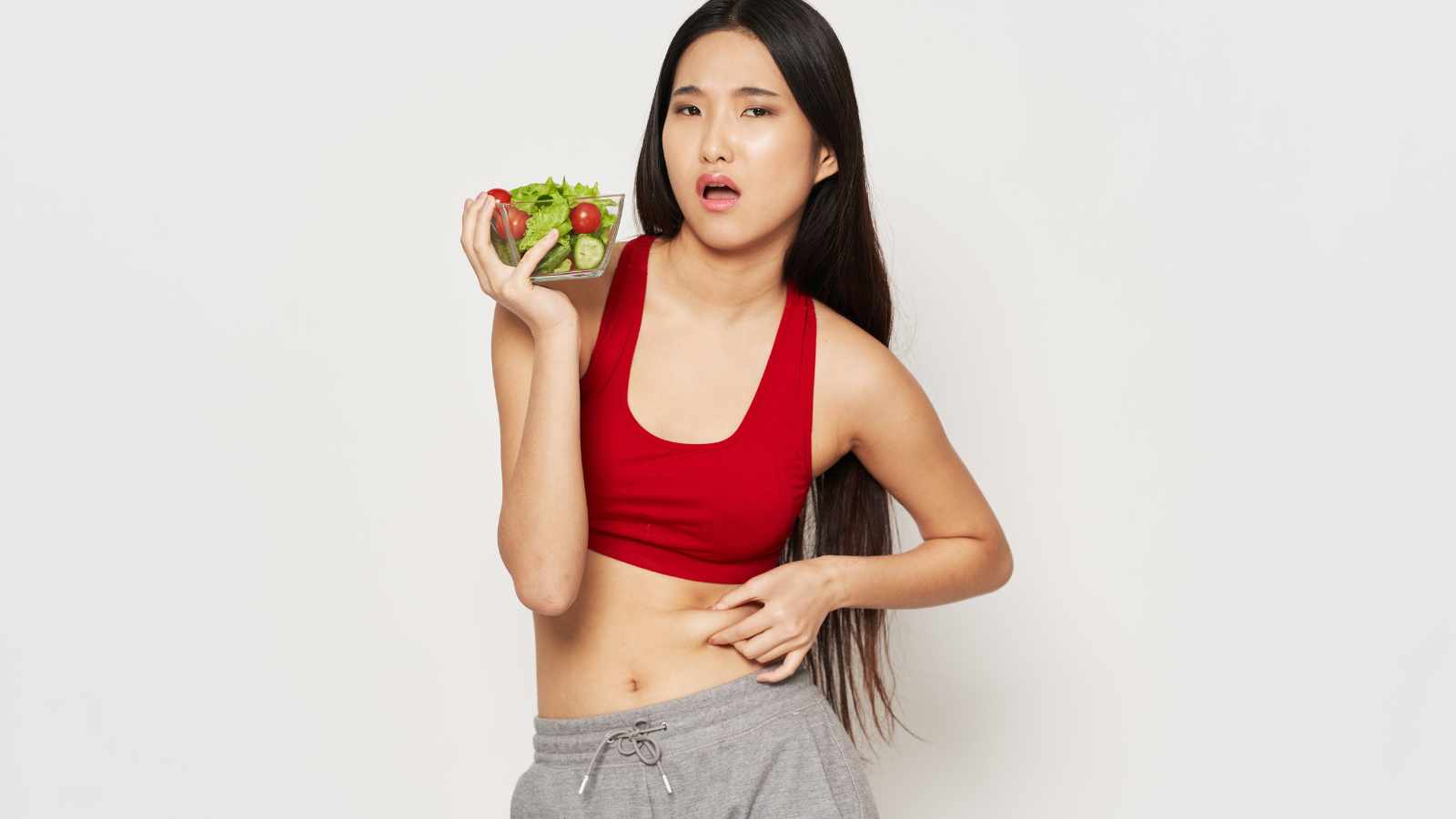 Woman with salad bowl squeezing her belly fat